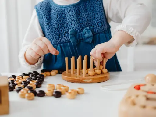 Niña con vestido azul jugando con cuentas de madera y un juego de encaje, parte de juegos para superar el mutismo selectivo.
