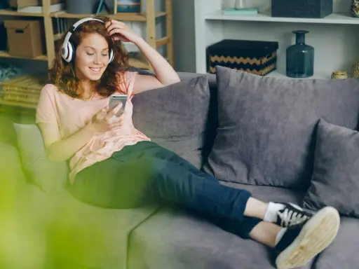 Dziewczyna z rudymi włosami słucha muzyki Indili, przeglądając telefon na kanapie. Jej uśmiech sugeruje, że to jej ulubiona love story.