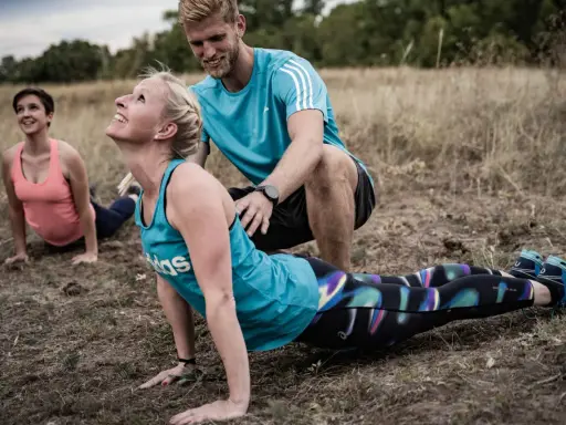 Ein Trainer unterstützt eine Frau bei einer Yoga-Übung im Freien. Das **Faszien Training** stärkt die Körpermitte.