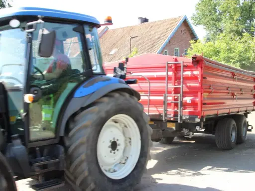 Rolnik z prawem jazdy na ciągnik prowadzi maszynę z czerwoną przyczepą.