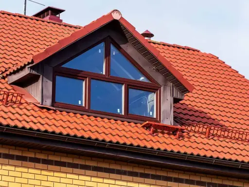 Ein Dachfenster mit dreieckigem Oberlicht und roten Ziegeln. Informieren Sie sich, was kostet eine gaube für Ihr Haus.