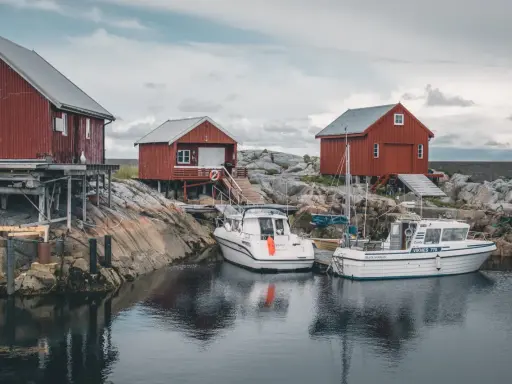 Norwegia: praca w norwegii dla par z zakwaterowaniem. Czerwone domki rybackie i łodzie przy skalistym brzegu.
