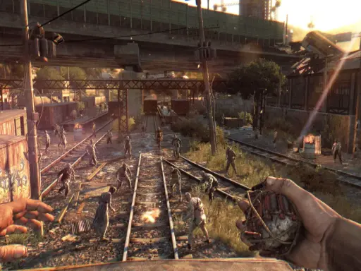 Gracz trzyma granat, otoczony przez hordę zombie na torach kolejowych. To scena z gry Dying Light, gdzie wymagania sprzętowe są kluczowe dla płynności rozgrywki.