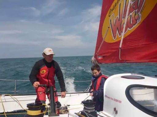 Franck-Yves Escoffier et un jeune garçon naviguent sur un voilier par temps ensoleillé.