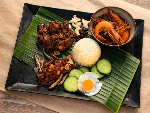 Nasi Lemak: Reis, scharfe Garnelen, frittierte Sardellen, Spiegelei, Gurkenscheiben, Cashewkerne und Rosinen auf Bananenblatt.