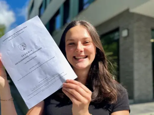 Stolze Schülerin mit Abiturzeugnis in der Hand. Sie fragt sich, wie viele Punkte für 0,9 Abi nötig sind.