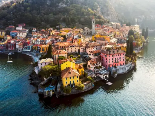 Färgstark by vid en sjö i norra Italien, med hus i gult, rosa och orange som klättrar uppför en sluttning.