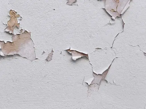 Texture d'un mur où la peinture se décolle comme du plastique, révélant des couches anciennes et la texture du plâtre.