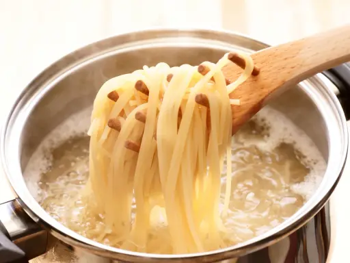 Une louche en bois retire des spaghettis bouillis à la perfection, juste al dente, d'une casserole d'eau bouillante.