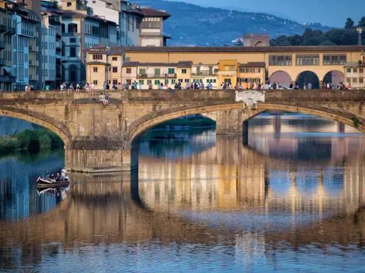 Le Ponte Vecchio à Florence, avec ses maisons colorées et ses reflets sur l'Arno. Une barque navigue paisiblement sous le pont.