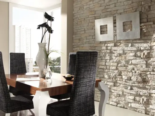 Comedor moderno con mesa de madera, sillas tapizadas y una pared con distintos tipos de revestimientos de piedra.