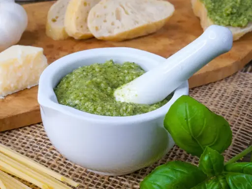 Frisches Basilikum-Pesto im Mörser, bereit zum Genießen. Dazu Brot, Parmesan und Pasta – so einfach ist basilikum pesto selber machen.