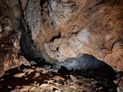 Wnętrze jaskini mylnej, z kamienistym dnem i skalnymi ścianami o rdzawym zabarwieniu, tworzącymi naturalne sklepienie.