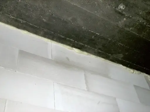 Piana montażowa, która jest rodzajem **elastomery**, uszczelnia połączenie między betonową belką a białymi bloczkami.