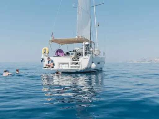 Erfahrungen, wenn du der Crew beitrittst: Ein Mann sitzt auf einer Yacht, während andere im Meer schwimmen.