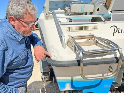 Un homme examine les dégâts sur le gelcoat d'un bateau. C'est quoi le gelcoat ? C'est la couche protectrice extérieure.