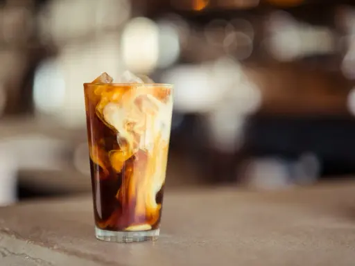 Ein Glas mit Eiswürfeln und cremiger Milch, die sich in dunklem Kaffee wirbelt. Perfekt für die Zubereitung von Cold Brew Coffee.