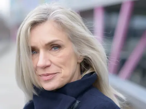 Donna con capelli bianchi e occhi azzurri, indossa un cappotto blu scuro. Un esempio di come vestirsi con i capelli bianchi.