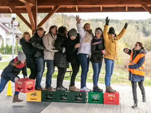 Uczestnicy zabawy, w ramach konkurencji sportowych dla dorosłych, tworzą łańcuch, balansując na skrzynkach po piwie.