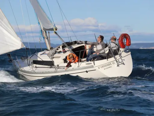Un bateau symphonie navigue sur des eaux bleues, trois personnes à bord profitent du soleil.