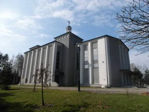 Nowoczesny kościół w Warszowicach, z charakterystycznymi pionowymi żłobieniami na fasadzie, pod błękitnym niebem.