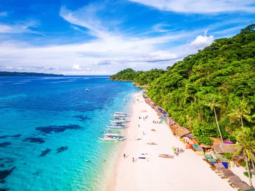 Piękna plaża na Filipinach w listopadzie. Turkusowa woda, biały piasek, palmy i łodzie. Idealna pogoda na wakacje.