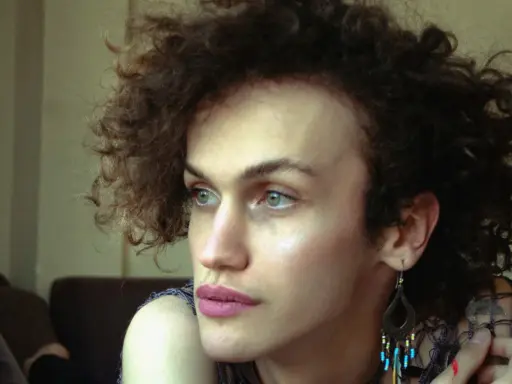 Portret osoby z kręconymi włosami, która zastanawia się nad przyczynami dysforii płciowej.