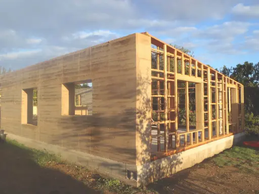 Construction d'une maison terre crue aux murs stratifiés, avec une ossature bois visible pour la suite.