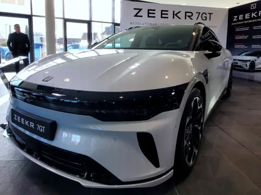 Ein Mann steht vor einem glänzenden, weißen Zeekr 7 GT in einem Ausstellungsraum. Das Auto hat eine markante schwarze Frontpartie.