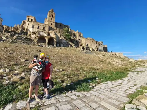 Coppia con cane visita le suggestive rovine di Craco vecchia, un borgo fantasma sotto un cielo azzurro.