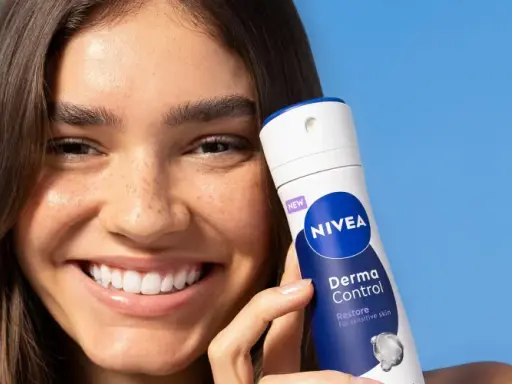 Donna sorridente con prodotto Nivea Derma Control, ideale per chi soffre di bruciore sotto le ascelle.