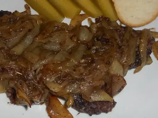 Pyszna kaszanka z patelni, duszona z cebulką, podana z ogórkiem kiszonym i kromką chleba.