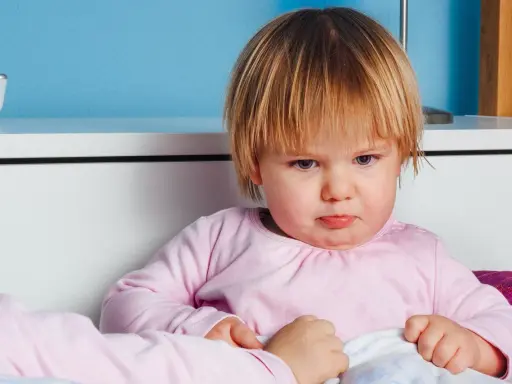 Smutna dziewczynka w różowej bluzce, być może z powodu nietolerancji laktozy, siedzi w łóżku.