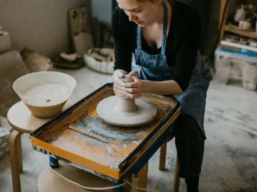 Jeune femme concentrée sur son apprentissage de l'artisanat de la poterie, façonnant l'argile sur un tour.