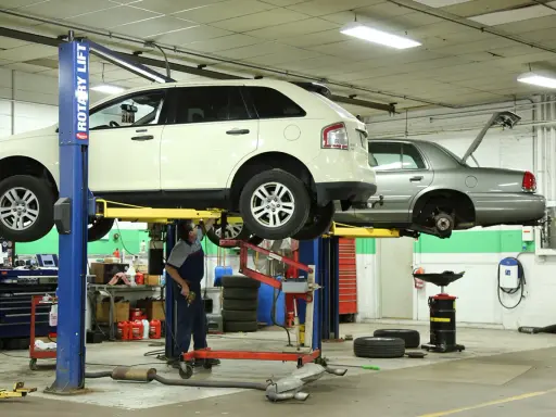 Mecánico trabajando en un taller con vehículos elevados, usando herramientas para neumáticos y otros equipos.