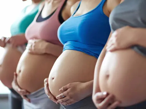 Fyra gravida kvinnor står sida vid sida och håller sina magar. En av dem, andfådd gravid, ler.