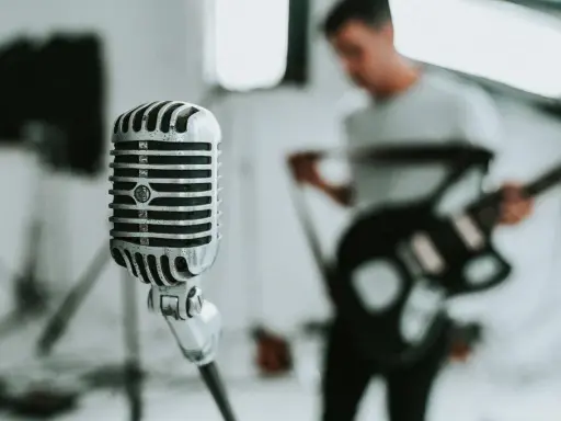 Retro mikrofon gotowy do uchwycenia niskich tonów głosu śpiewaka, podczas gdy w tle muzyk gra na gitarze.