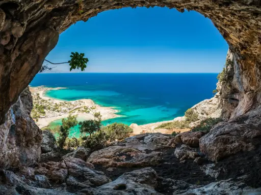Widok z jaskini na turkusowe morze i plażę. Idealna kreta pogoda w kwietniu, słońce i błękitne niebo.