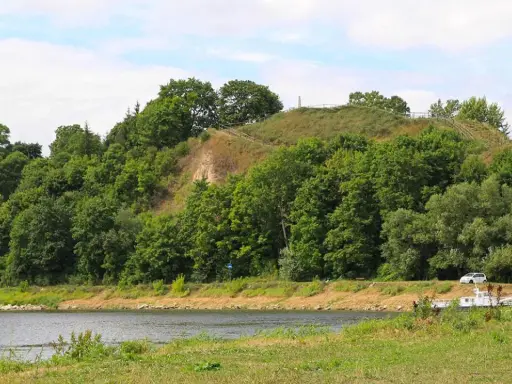 Zielona skarpa nad rzeką, na szczycie której widać ścieżki i ogrodzenie. To góra zamkowa w Drohiczynie, miejsce pełne historii.
