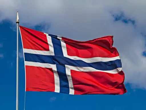 Norweska flaga powiewa na wietrze. W tle błękitne niebo z chmurami. Takie są prace, gdy jest piękna pogoda.