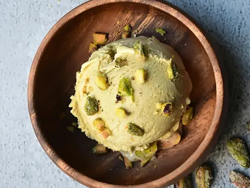 Cremoso helado de pistacho con trozos de pistacho en un cuenco de madera.