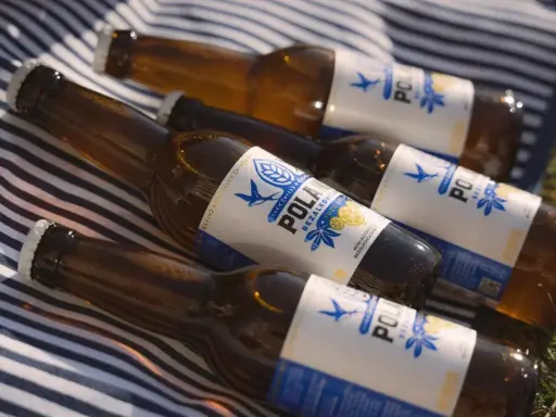 Butelki piwa POLAN z napisem "BEZALKOHOLOWE" leżą na kocu w paski. To piwo ma 0 alkoholu, idealne na upalne dni.