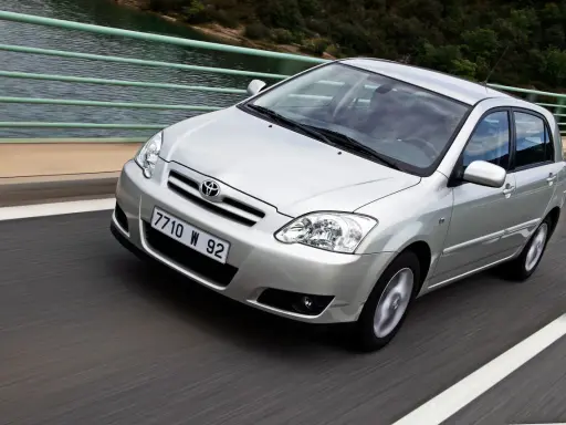 Srebrna Toyota Corolla 2004 na moście, z widokiem na wodę i las.
