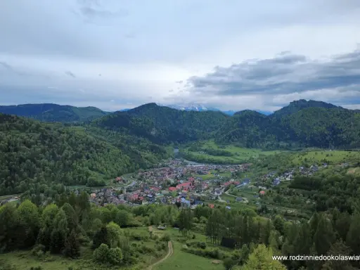 Widok na malowniczą dolinę z miasteczkiem Szczawnica. W oddali góry, a na pierwszym planie zielone wzgórza. To idealne miejsce na odkrywanie szczawnickich atrakcji.