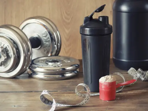 Pesas, batidora y cuchara con proteína en polvo. Ideal para saber cuándo tomar batido de proteínas y optimizar tu entrenamiento.