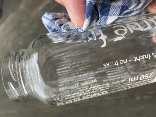 Mit einem Tuch wird das "true fruits" Schrift entfernt. Die Flasche ist aus Glas und hat einen Pfandaufdruck.
