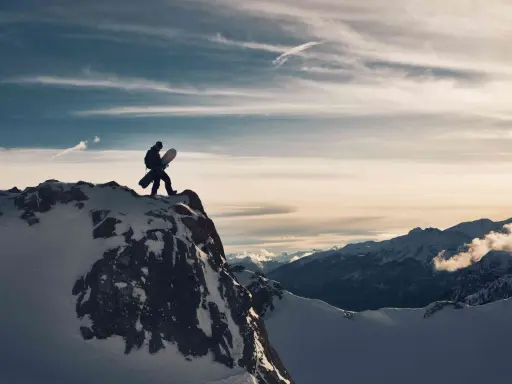 Sylwester w Alpach: snowboardzista na szczycie góry, gotowy na zjazd. W tle majestatyczne, ośnieżone szczyty i dramatyczne chmury.