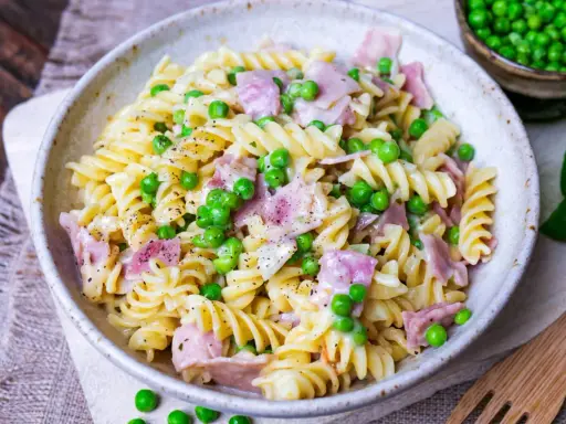 Fusilli-Nudeln mit Erbsen und Schinken in einer cremigen schinken sahne sauce, bestreut mit schwarzem Pfeffer.