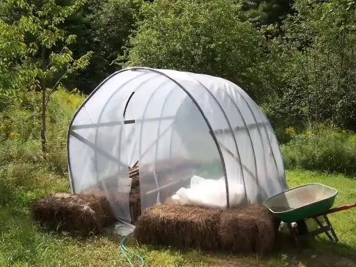 Un invernadero listo para el huerto de verano, con fardos de paja y carretilla a los lados.