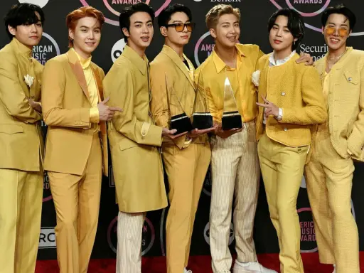 Medlemmar av BTS poserar glatt på röda mattan, klädda i matchande gula outfits och håller sina American Music Awards-troféer.